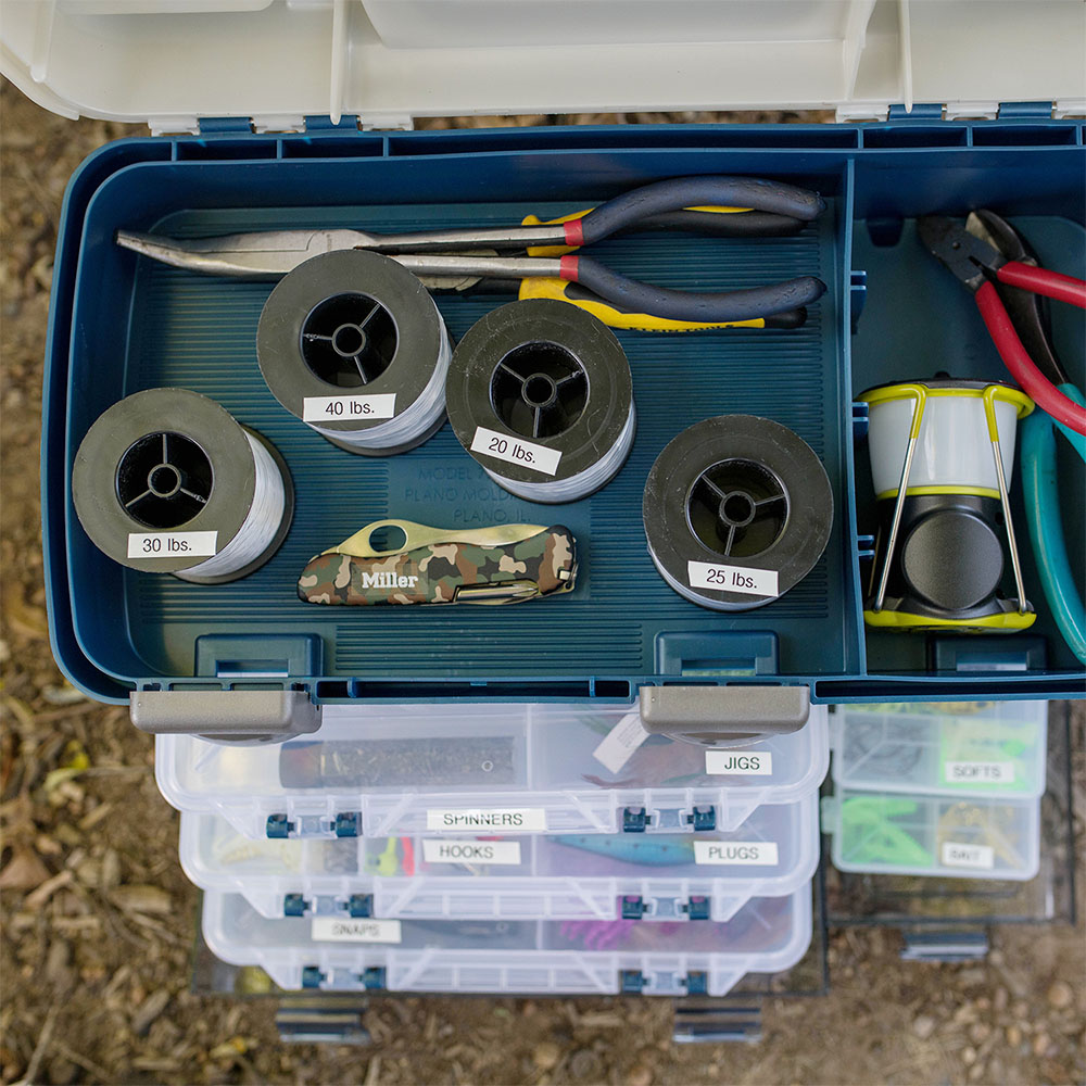 Caja de aparejos de pesca con carretes y compartimentos identificados mediante etiquetas Brother TZe-231.
