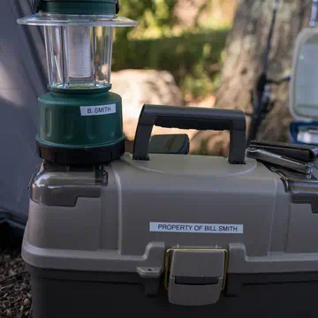 Linterna de camping y caja de herramientas al aire libre, identificadas con etiquetas blancas con los textos “B. Smith” y “Property of Bill Smith”.