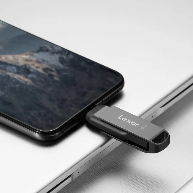 Pendrive Lexar JumpDrive Dual Drive D400 de 256 GB color gris oscuro con el conector USB-C insertado en un smartphone, sobre la carcasa de una laptop