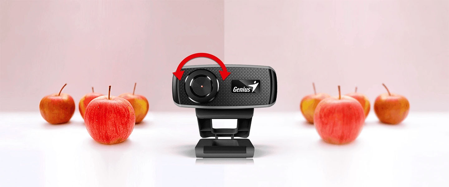Webcam Genius FaceCam 1000X rodeada de manzanas con una flecha roja indicando la capacidad de enfoque manual de la lente