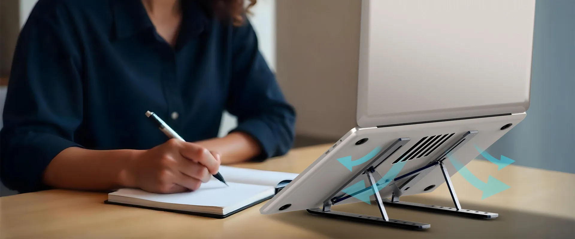 Persona en un escritorio con una notebook sobre el soporte G-Stand M250, destacando la ventilación con flechas de flujo de aire.