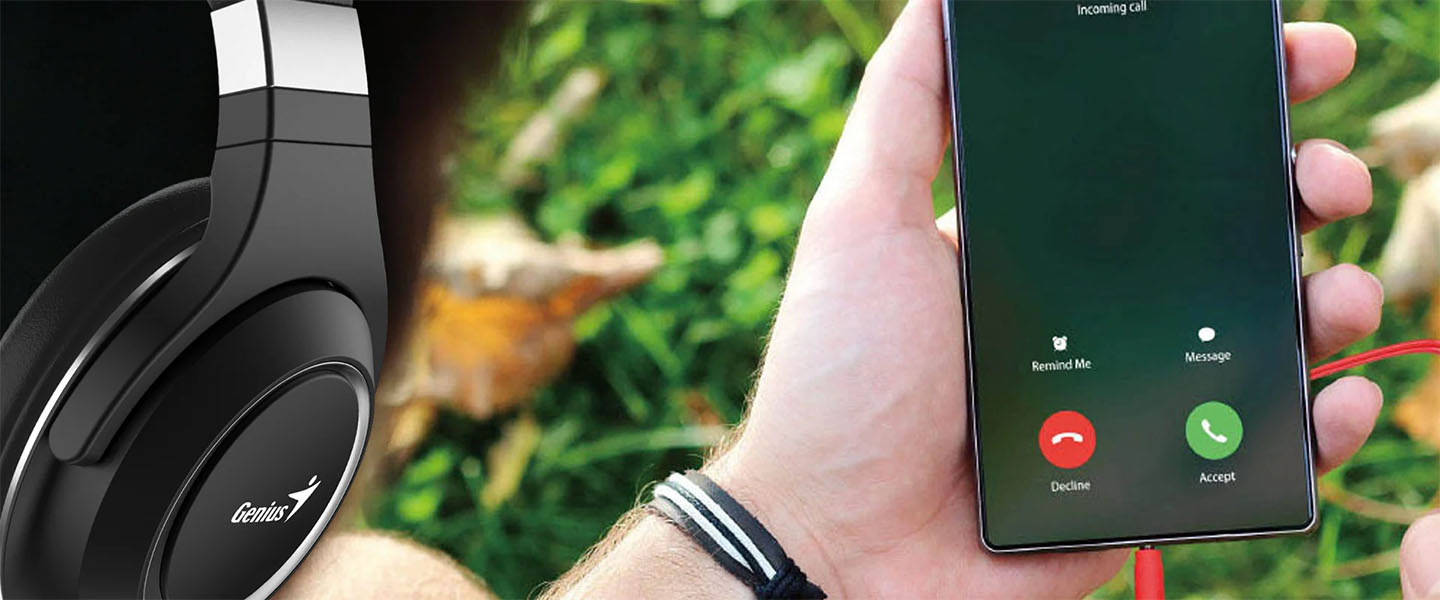 La imagen muestra unos auriculares Genius HS-610 negros en primer plano a la izquierda, y una mano sosteniendo un teléfono móvil a la derecha. El teléfono muestra una pantalla de llamada entrante con opciones para Recordarme, Mensaje, Rechazar y Aceptar. El fondo es un área verde con hojas.