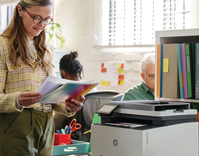 Mujer revisando documentos a color impresos junto a la impresora multifunción HP Color LaserJet Pro MFP 3303fdw en una oficina con más gente