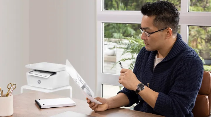 Hombre revisando impresión de la multifuncional HP LaserJet M141W en oficina minimalista.