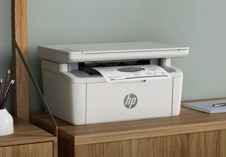 Impresora multifunción HP LaserJet M141W blanca, imprimiendo un documento sobre escritorio de madera.