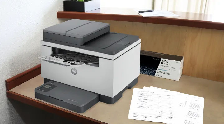 HP LaserJet M236sdw imprimiendo, con cartucho de tóner 136A y documentos apilados, ideal para oficina