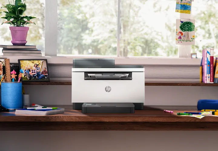 Impresora multifunción HP LaserJet M236sdw blanca en un escritorio de madera para estudio u hogar, lista para imprimir