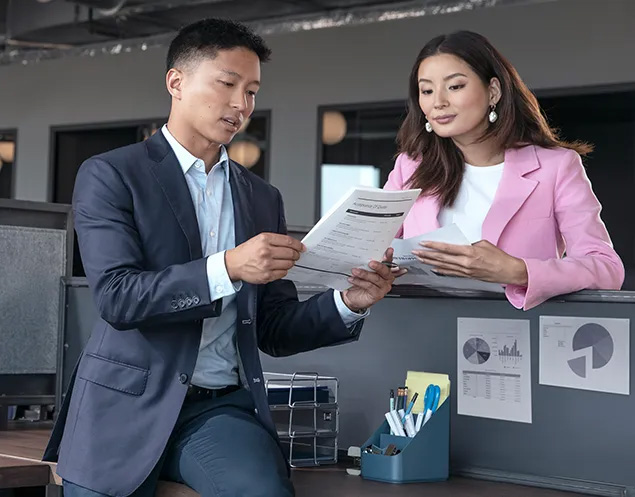 Dos profesionales, un hombre y una mujer, revisando un documento impreso en una oficina, ilustrando la velocidad de impresión para equipos de trabajo.