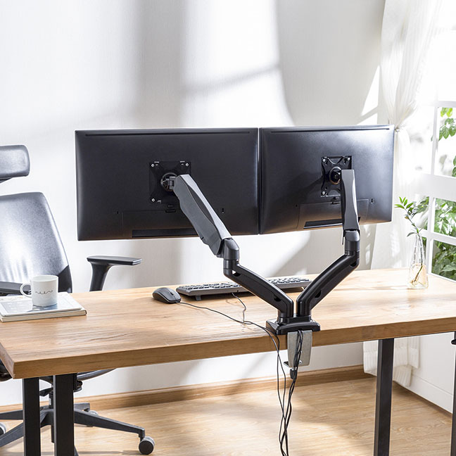 Vista trasera de un escritorio de madera con dos monitores negros montados en un Soporte hidráulico doble para pantallas planas y curvas Intelaid IT-DGB2U