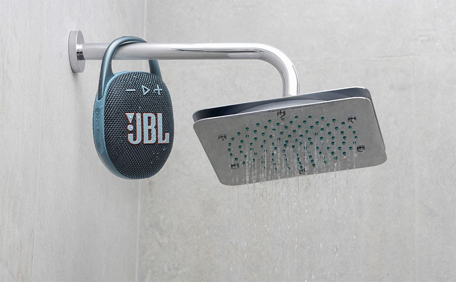Parlante Bluetooth JBL Clip 5 azul marino colgado del brazo de una ducha que está encendida.