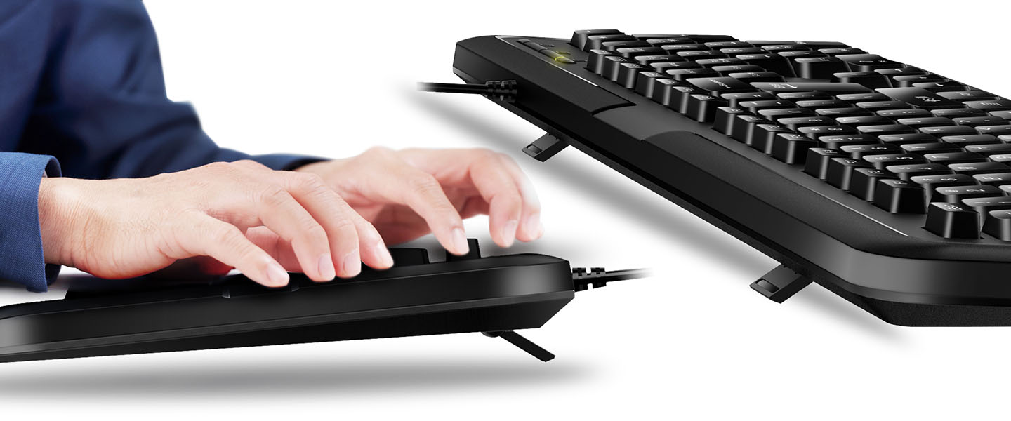 Teclado Genius KB-118 color negro, siendo tecleado por manos sobre un fondo blanco.