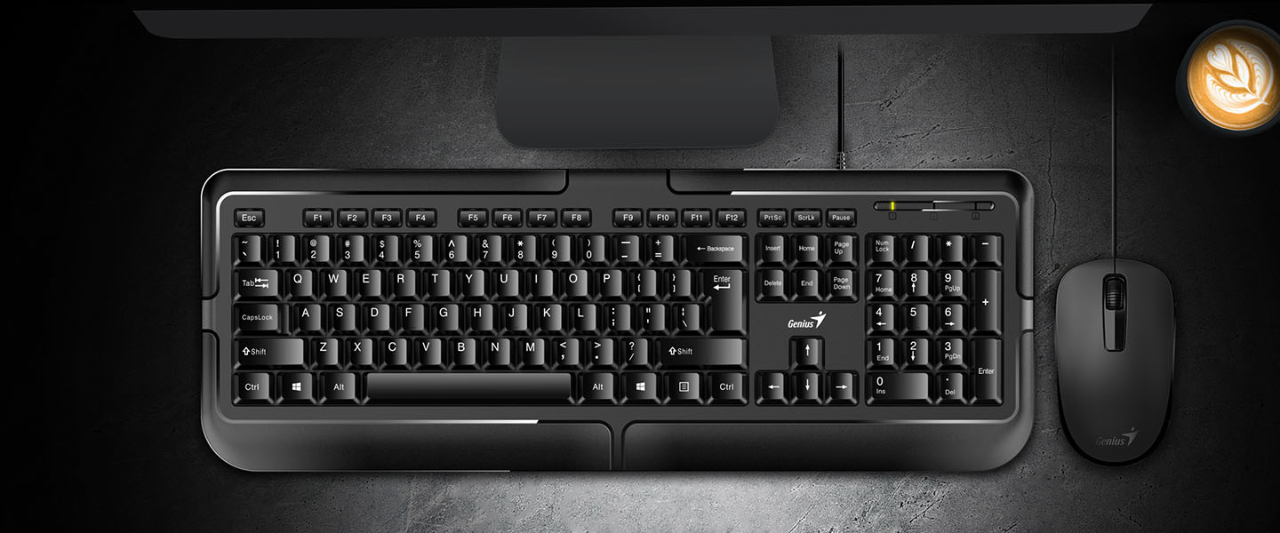 Vista aerea de un Teclado Genius KB-118 color negro y un mouse descansando sobre una mesa oscura, junto a una taza de café y parte de un monitor.