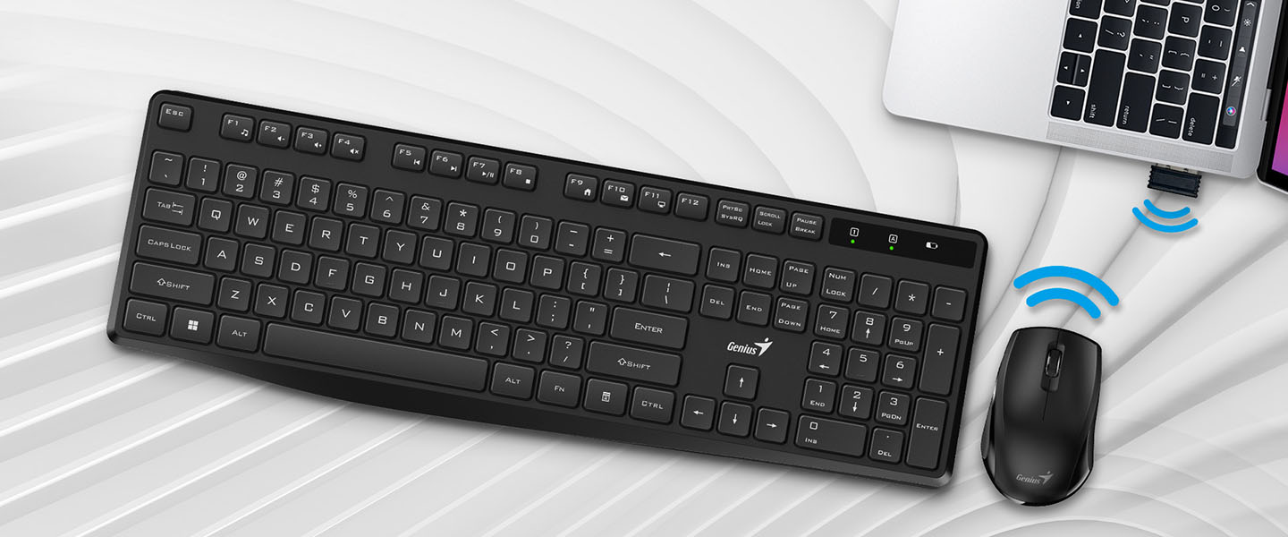Un Combo de Teclado y Mouse inalámbrico Genius KM-8206S sobre una superficie blanca y gris. En el lado derecho, se vislumbra parcialmente un portátil.