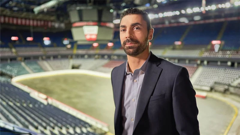Ziad Mehio está de pie en un estadio con una chaqueta deportiva azul marino.