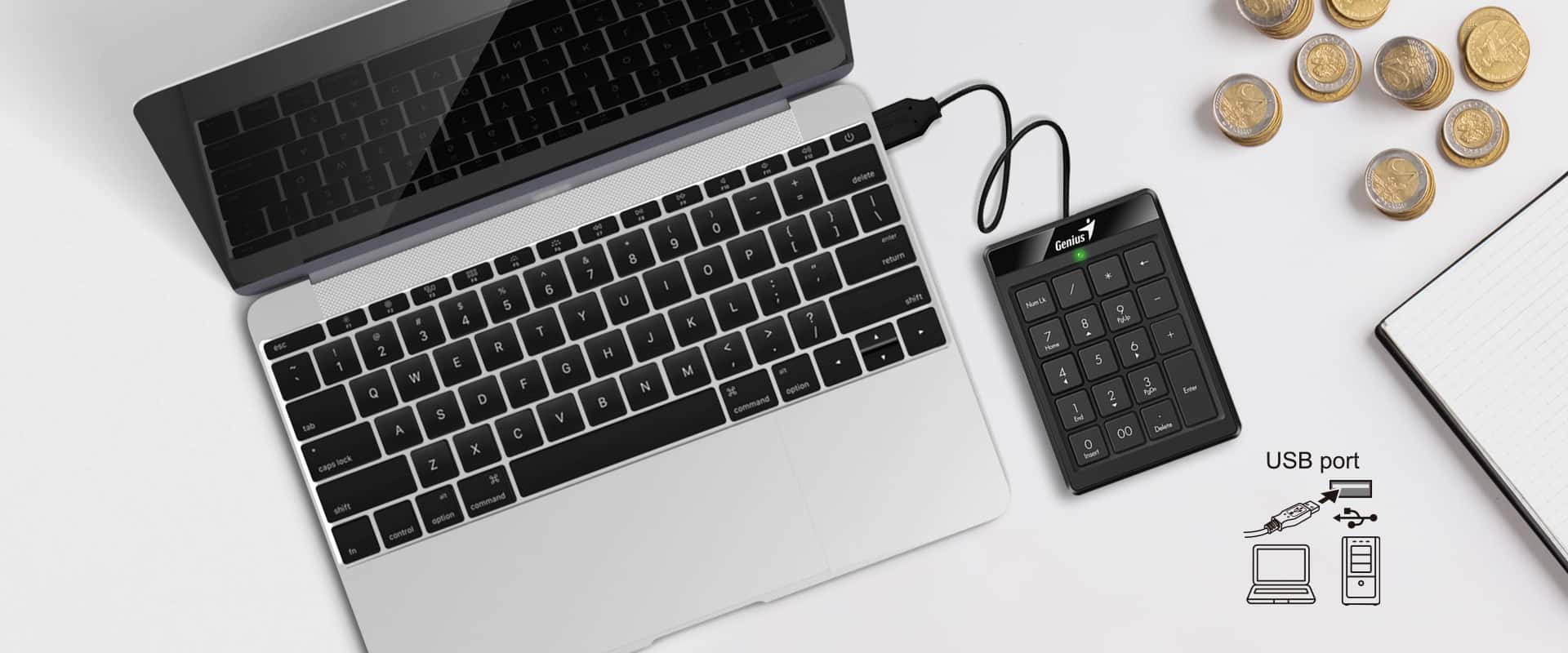 Un teclado numérico negro Genius Numpad 110 está conectado a un puerto USB de una computadora portátil plateada. El teclado numérico se encuentra a la derecha de la computadora portátil sobre una superficie blanca. En la esquina superior derecha hay varias monedas de euro apiladas y un cuaderno blanco parcialmente visible. En la esquina inferior derecha se muestra un diagrama que ilustra la conexión USB del teclado numérico a una computadora portátil o de escritorio.