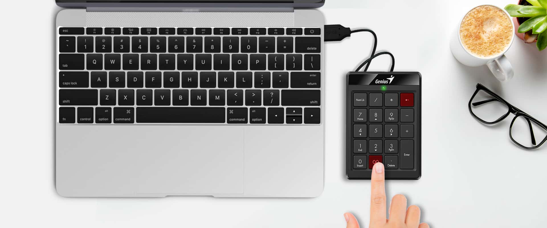 Mano usando un Teclado Numérico Compacto Genius NumPad 110 conectado a una notebook, al lado de una taza de café y anteojos.