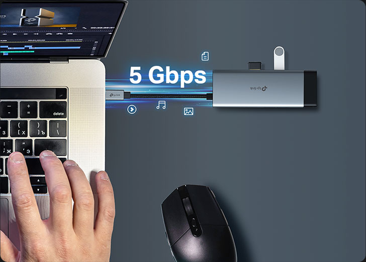 Hub USB-C TP-Link UH6120C plateado conectado a una notebook, destacando la velocidad de transferencia de datos de 5 Gbps de sus puertos USB 3.0. Una mano teclea en el portátil que tiene un software de edición de video abierto. El hub tiene conectados una Pendrive USB y un dongle USB.