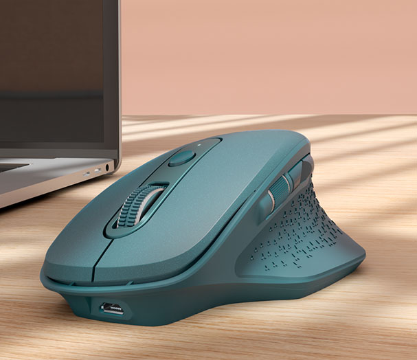 Un Mouse inalámbrico recargable Trust Ozaa - Azul, apoyado sobre una mesa de madera. En el fondo, se vislumbra una laptop parcialmente visible.