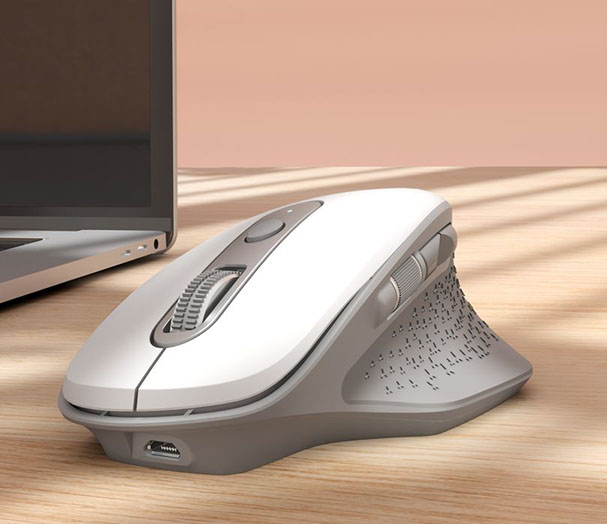 Un Mouse inalámbrico recargable Trust Ozaa - Blanco, apoyado sobre una mesa de madera. En el fondo, se vislumbra una laptop parcialmente visible.