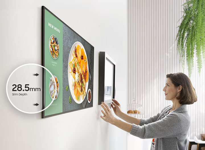Una pantalla Samsung Smart Signage montada en pared, con indicador de 28.5 mm de profundidad slim y contenido de menú en la pantalla