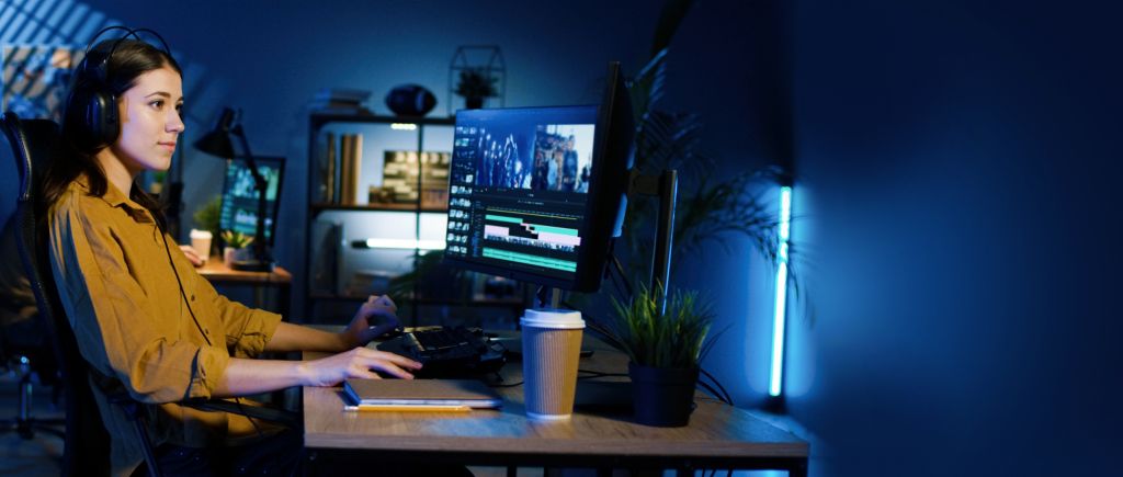 Persona usando auriculares y trabajando en una PC de escritorio con doble monitor en un ambiente iluminado con luces LED azules