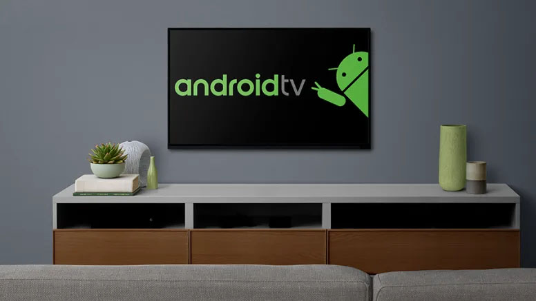 Televisor montado en una pared gris que muestra el logo de Android TV en la pantalla, sobre un mueble de TV moderno.