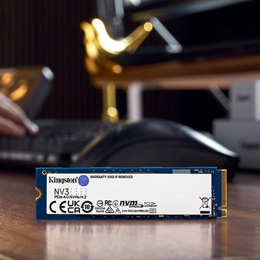 Un SSD NV3 NVMe M.2 está de pie en el borde del escritorio, con manos sobre un teclado en el fondo.