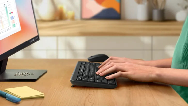 Persona usando el teclado del Logitech Bluetooth® Wireless Combo MK250 sobre un escritorio de madera junto a un monitor y notas adhesivas