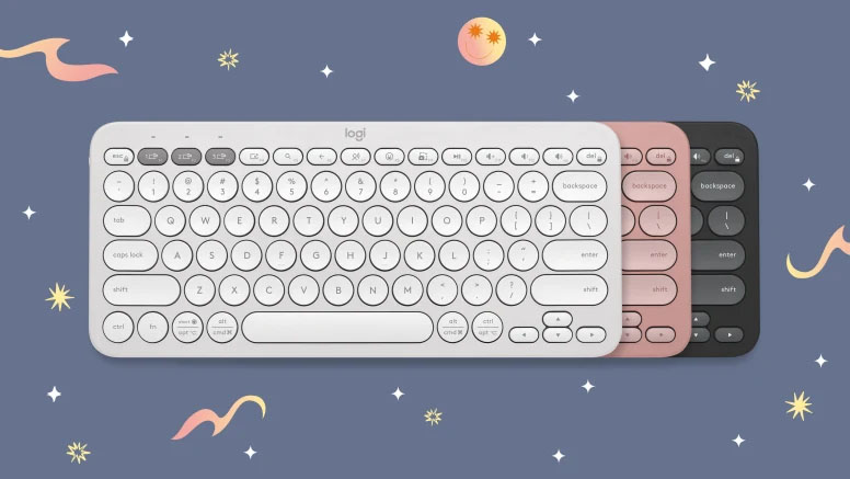Tres teclados Logitech Pebble Keys 2 K380s apilados, en colores blanco, rosado y negro, sobre un fondo nocturno con estrellas y nubes.