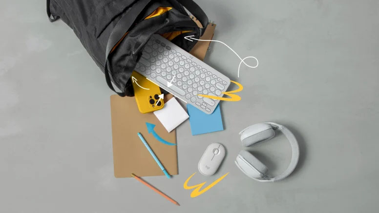 Un teclado Logitech Pebble Keys 2 K380s blanco sale de una mochila negra junto con otros accesorios como un mouse, auriculares y un celular.