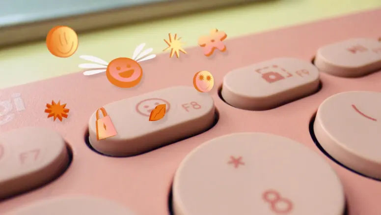 Primer plano de un teclado Logitech Pebble Keys 2 K380s rosado, mostrando algunas de sus teclas con emojis y funciones especiales.