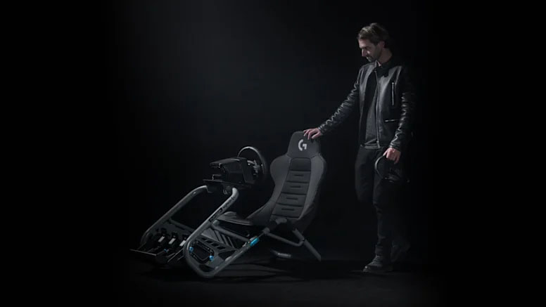 Un hombre de pie junto a un asiento de simulador de carreras Logitech G que tiene un volante y pedalera colocados, en un fondo oscuro