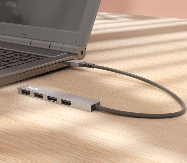 Hub USB mini de aluminio Trust Halyx con 4 puertos USB-A conectado a una notebook sobre un escritorio de madera