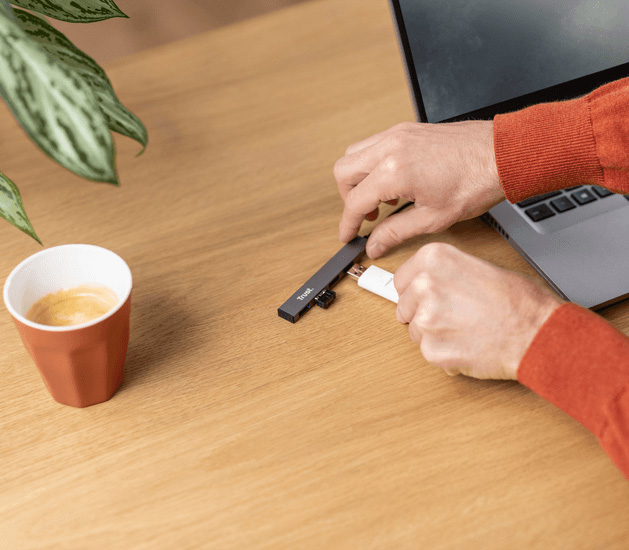 Persona conectando dispositivos al hub USB mini de aluminio Trust Halyx de 4 puertos sobre un escritorio junto a una notebook