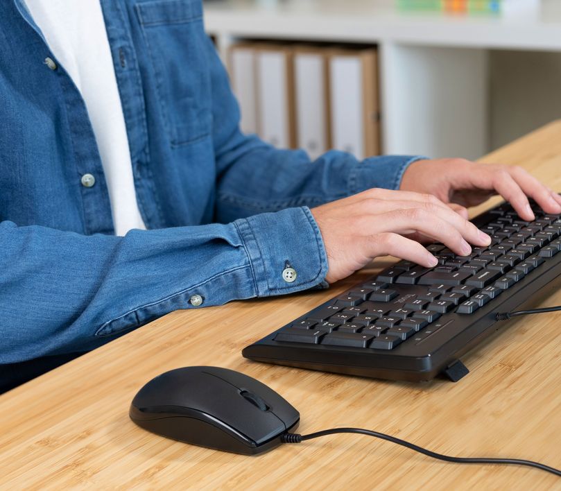 Persona utilizando un Combo de Teclado y Mouse Trust Primo sobre una mesa de madera.