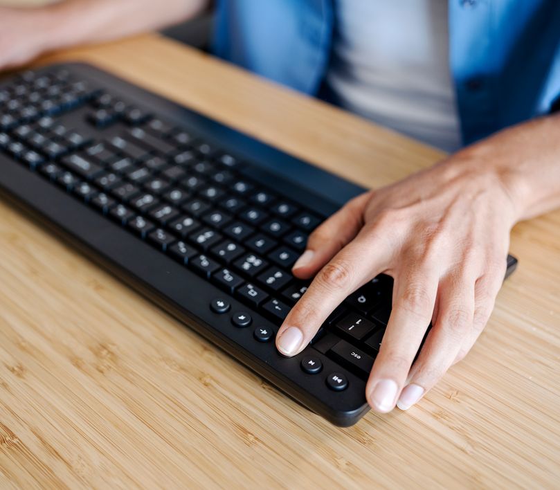 Mano sobre el teclado inalámbrico de un Combo de Teclado y Mouse inalámbrico Trust Trezo Comfort en una mesa de madera, presionando una tecla.