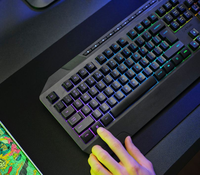 Teclado Gaming Iluminado Trust GXT 836 Evocx sobre una mesa, con una mano presionando una tecla.