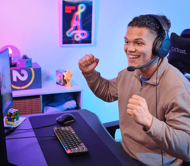 Persona usando el teclado Trust GXT 867 Acira en un escritorio gaming mientras juega con auriculares puestos