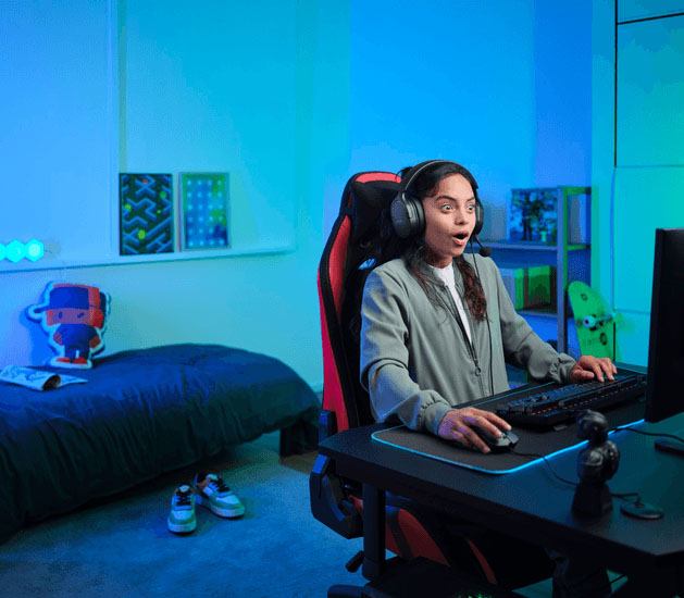 Alguien con uno Auriculares Gaming 7.1 USB Trust GXT 490 Fayzo y expresión de sorpresa, jugando en un setup gamer con luces de colores en un dormitorio.