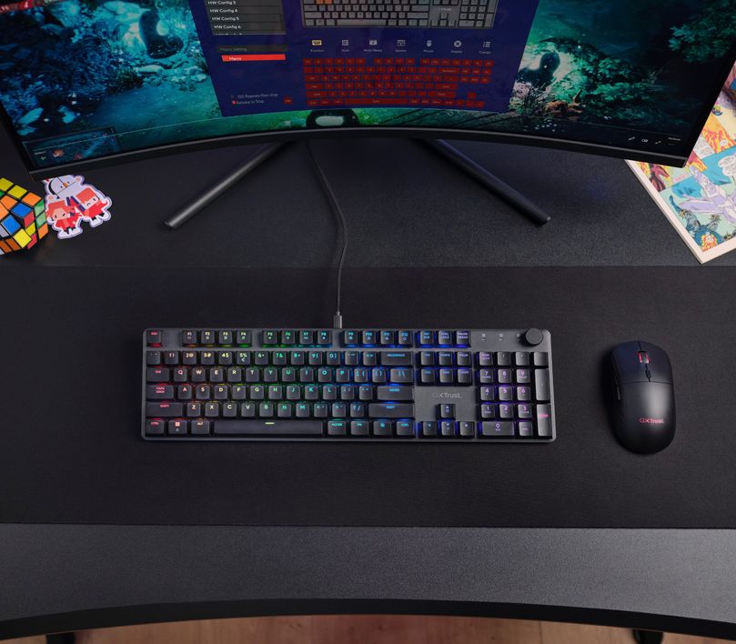 Vista superior del Teclado mecánico prémium Trust GXT 866 Torix, sobre un mousepad negro en un escritorio, frente a un monitor