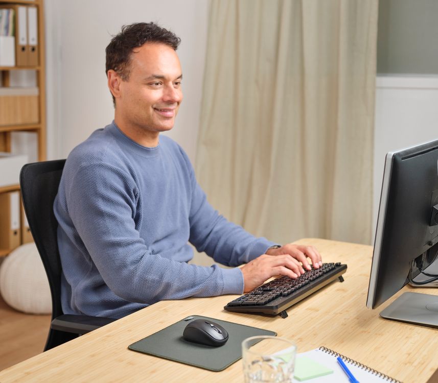 Persona utilizando una computadora con un Combo de teclado y mouse inalámbricos y silenciosos Trust Ody II en un escritorio organizado dentro de una oficina en casa.