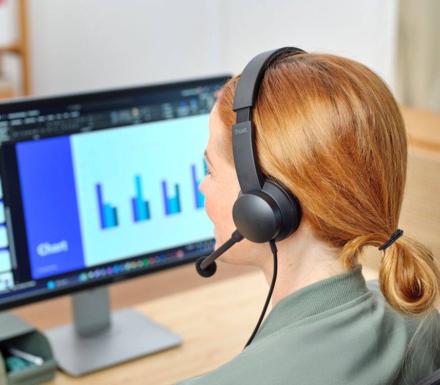 Una persona con auriculares USB-ENC para PC Trust Ayda está sentada frente a una computadora portátil.