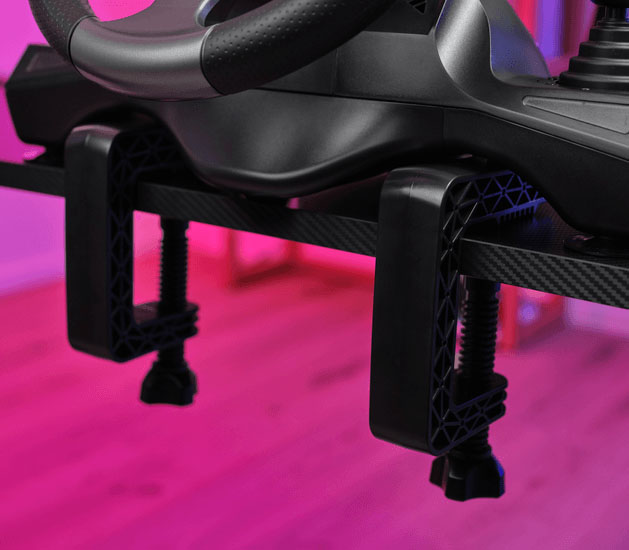 Primer plano del sistema de montaje del volante Trust GXT 289 Movi, mostrando las dos mordazas de sujeción ajustables atornilladas a un escritorio de textura tipo fibra de carbono