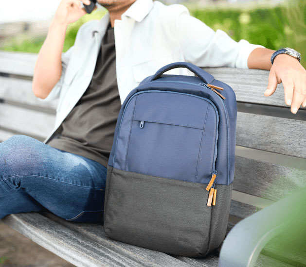 Hombre sentado en un banco hablando por teléfono junto a la mochila para notebook Trust Lisboa 16 pulgadas en color azul, destacando su estilo moderno y diseño urbano.