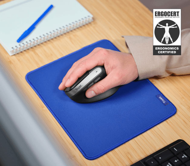 Mano usando el mouse ergonómico inalámbrico Trust Bayo II negro sobre un pad para mouse azul en un escritorio de madera. Se ve el logo de ERGOCERT de Certificado Ergonómico.