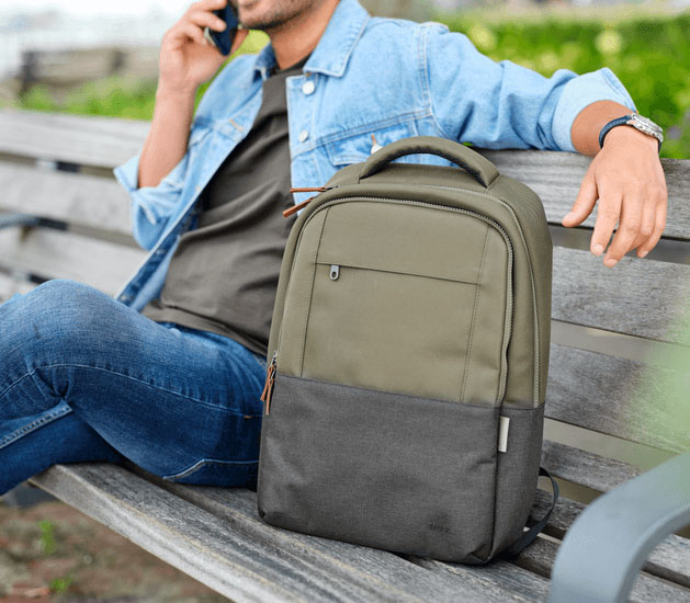 Hombre sentado en un banco hablando por teléfono junto a la mochila para notebook Trust Lisboa 16 pulgadas en color verde, destacando su estilo moderno y diseño urbano.