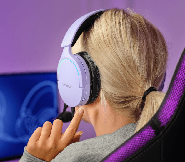 Primer plano de una persona usando Auriculares Gaming 7.1 USB Trust GXT 490P Fayzo Morados con micrófono, mirando un monitor de juego desenfocado.