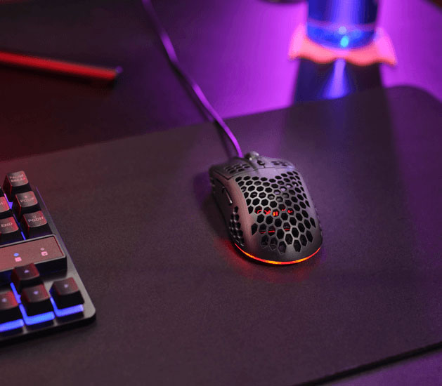 Mouse gaming Trust GXT 928 Helox ultraliviano con diseño perforado e iluminación RGB sobre un escritorio gamer