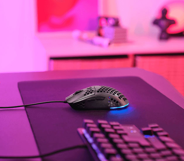 Mouse gaming Trust GXT 928 Helox ultraliviano con diseño perforado e iluminación RGB azul sobre un escritorio gamer