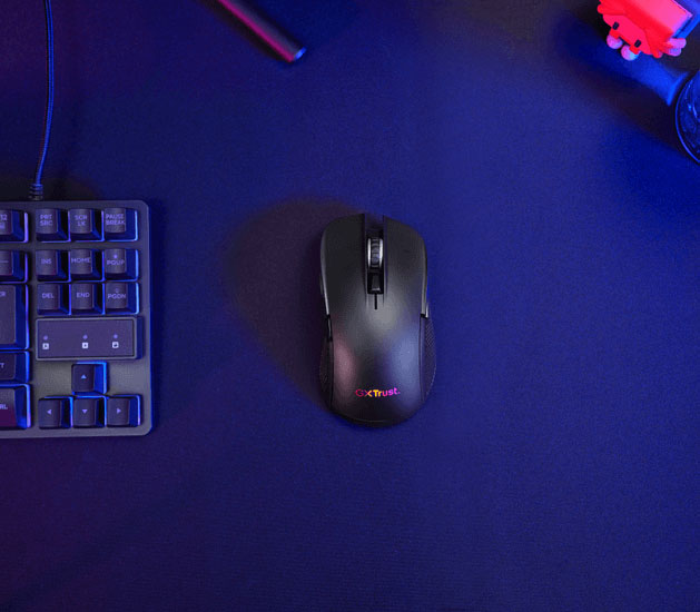Mouse gaming inalámbrico multidispositivo Trust GXT 931 Ybar negro visto desde arriba sobre una superficie oscura, con parte de un teclado al lado.